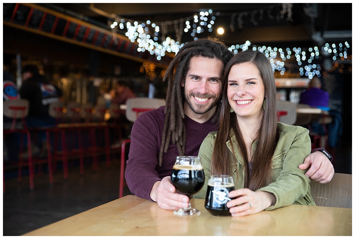 couple holding glasses for their engagement session at red leg brewery in colorado springs