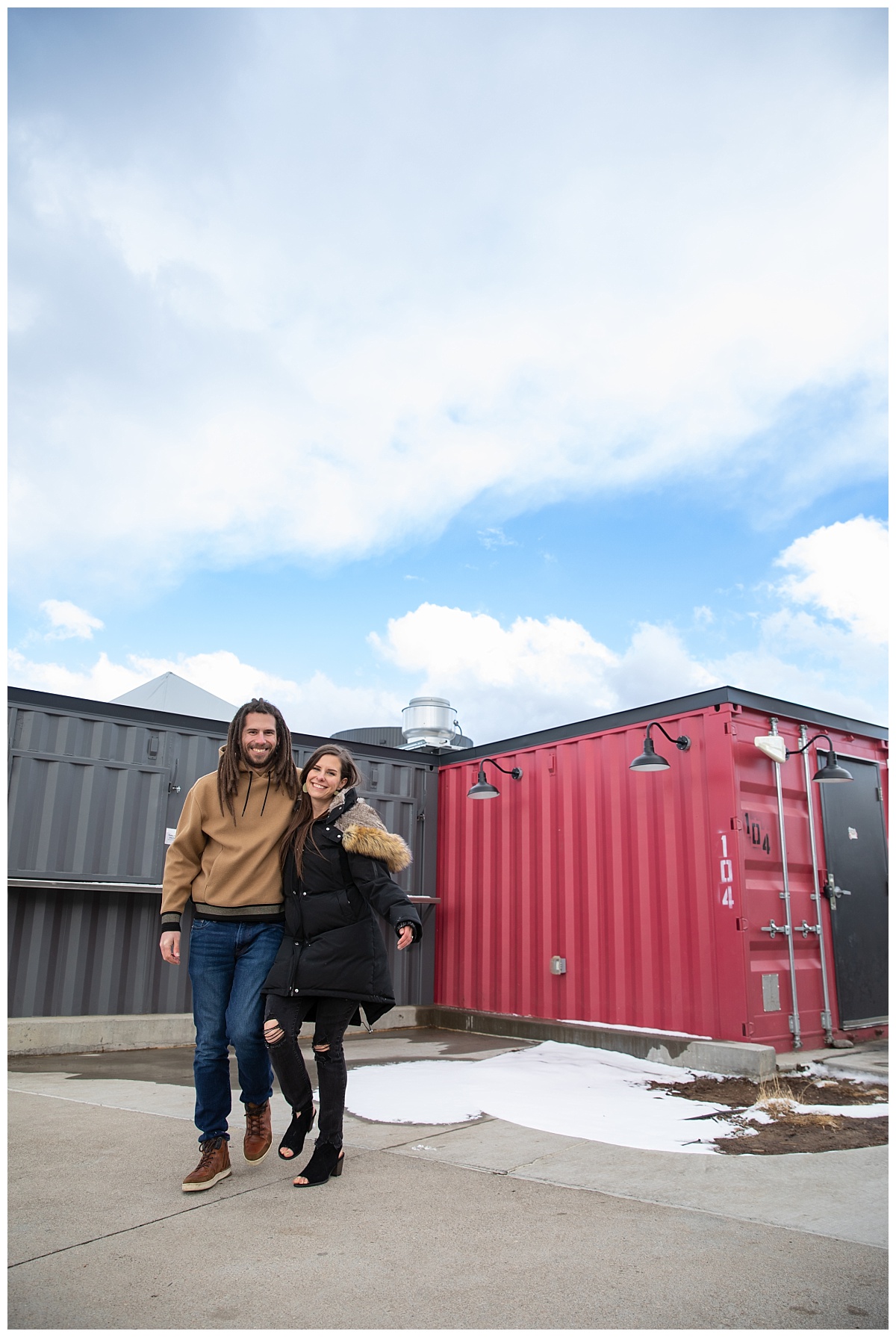 couple walking in front of storage containers for their engagement session